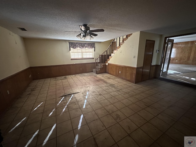 tiled spare room featuring ceiling fan, wood walls, and a textured ceiling