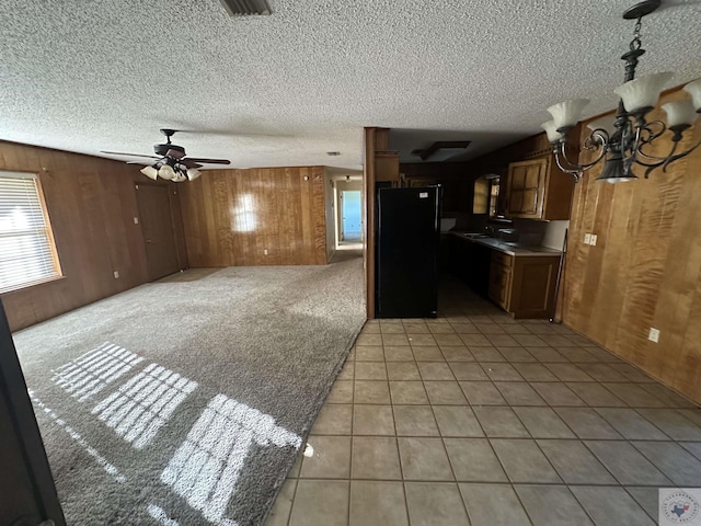 kitchen with black refrigerator, sink, light tile patterned flooring, ceiling fan with notable chandelier, and wooden walls