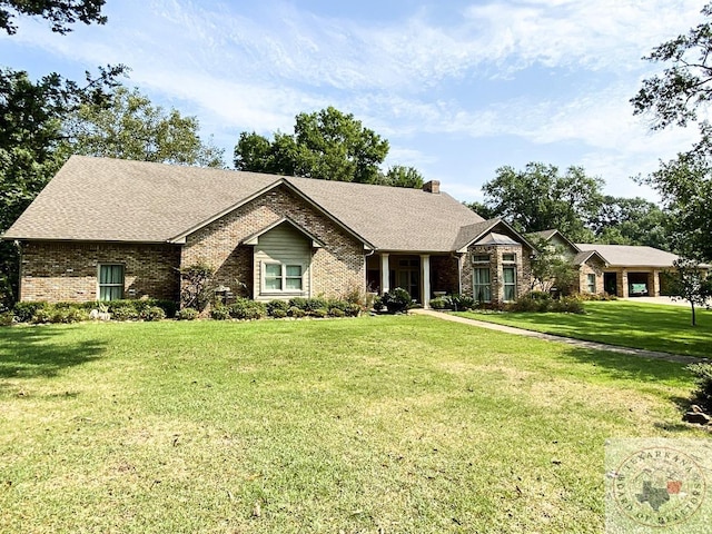 view of front of property with brick siding, a chimney, a front lawn, and roof with shingles