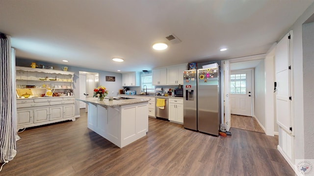 kitchen with appliances with stainless steel finishes, white cabinetry, sink, a kitchen island, and dark wood-type flooring