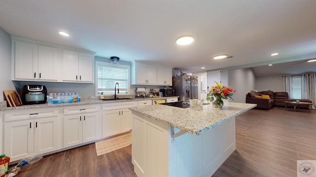 kitchen with appliances with stainless steel finishes, a kitchen island, white cabinetry, dark hardwood / wood-style flooring, and sink