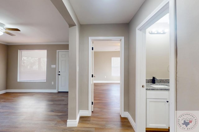 hall featuring light wood-style flooring, baseboards, and a sink