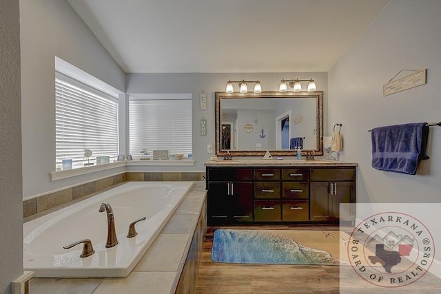 bathroom featuring vanity, tiled tub, and lofted ceiling