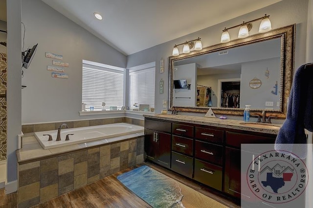 bathroom featuring hardwood / wood-style floors, a relaxing tiled tub, lofted ceiling, and vanity