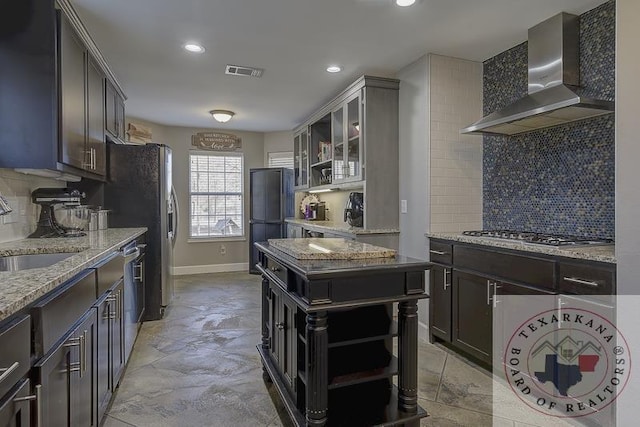 kitchen featuring wall chimney exhaust hood, tasteful backsplash, light stone countertops, and stainless steel appliances