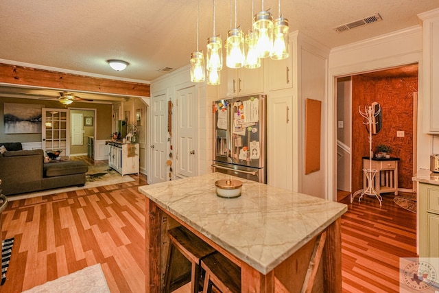 kitchen featuring pendant lighting, high quality fridge, a center island, a textured ceiling, and crown molding