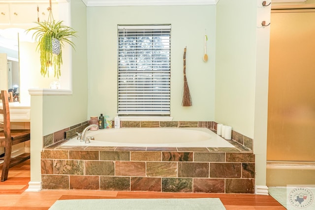 bathroom featuring wood-type flooring, tiled tub, ornamental molding, and a healthy amount of sunlight