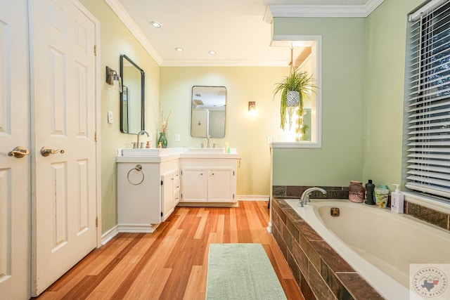 bathroom with a relaxing tiled tub, hardwood / wood-style floors, vanity, and crown molding