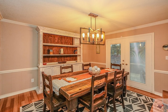 dining space with hardwood / wood-style flooring, an inviting chandelier, french doors, and ornamental molding