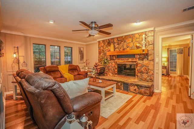 living room featuring light hardwood / wood-style floors, ceiling fan, ornamental molding, and a stone fireplace