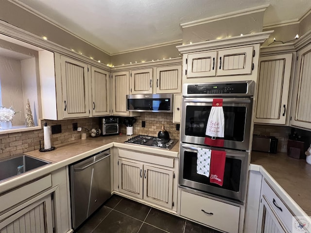 kitchen with dark tile patterned floors, stainless steel appliances, tasteful backsplash, cream cabinets, and crown molding