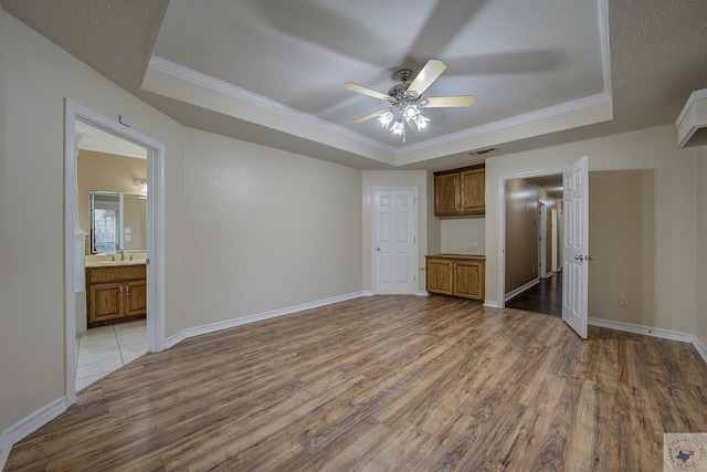 unfurnished bedroom with connected bathroom, sink, ornamental molding, a raised ceiling, and light hardwood / wood-style flooring