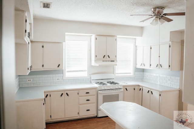 kitchen with ceiling fan, white range with gas stovetop, backsplash, white cabinets, and dark hardwood / wood-style floors