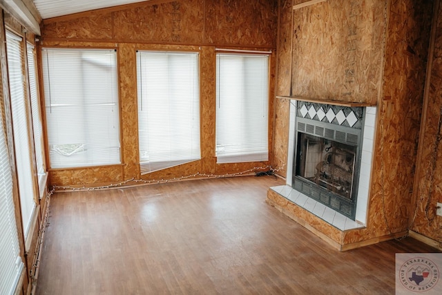 unfurnished living room with wood-type flooring, a tiled fireplace, and vaulted ceiling