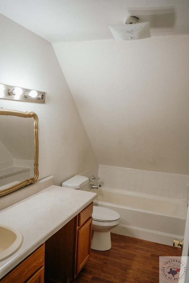 bathroom featuring lofted ceiling, wood-type flooring, vanity, toilet, and a washtub