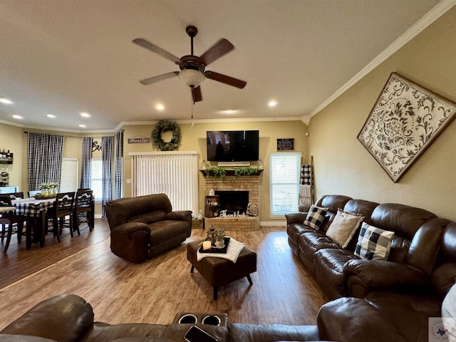 living room with recessed lighting, wood finished floors, a ceiling fan, ornamental molding, and a brick fireplace