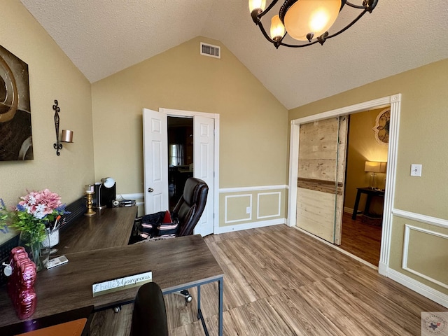 home office featuring a textured ceiling, a chandelier, wood finished floors, visible vents, and vaulted ceiling