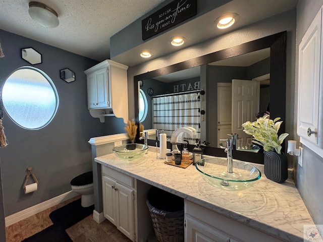 full bath with a textured ceiling, a sink, toilet, and baseboards