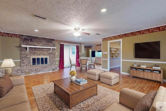 living room with a fireplace, a textured ceiling, light hardwood / wood-style flooring, and ceiling fan