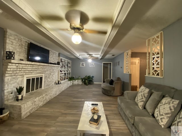 living room with ceiling fan, beamed ceiling, a fireplace, and wood-type flooring