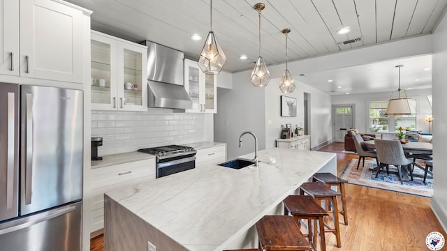 kitchen featuring wall chimney exhaust hood, stainless steel appliances, light wood finished floors, a sink, and visible vents