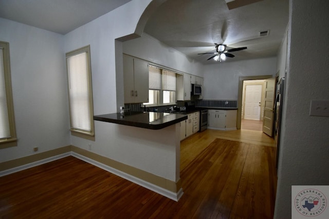 kitchen featuring hardwood / wood-style floors, appliances with stainless steel finishes, white cabinets, kitchen peninsula, and ceiling fan