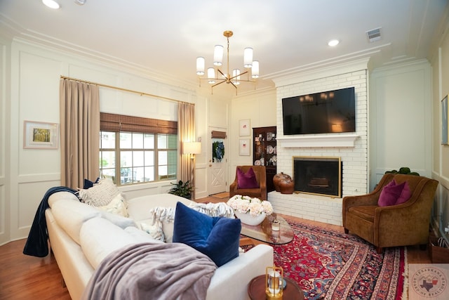 living room with a brick fireplace, hardwood / wood-style flooring, ornamental molding, and a chandelier