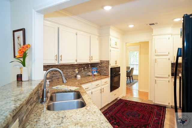 kitchen with sink, white cabinetry, light tile patterned floors, light stone counters, and black appliances