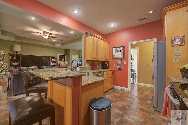 kitchen featuring kitchen peninsula, light brown cabinetry, sink, a kitchen bar, and stainless steel refrigerator