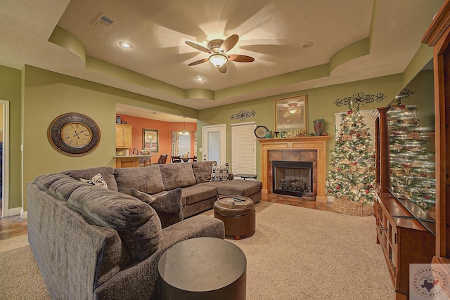 carpeted living room with ceiling fan, a fireplace, and a tray ceiling