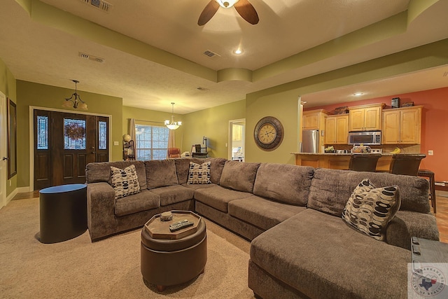 living room featuring ceiling fan with notable chandelier and a tray ceiling