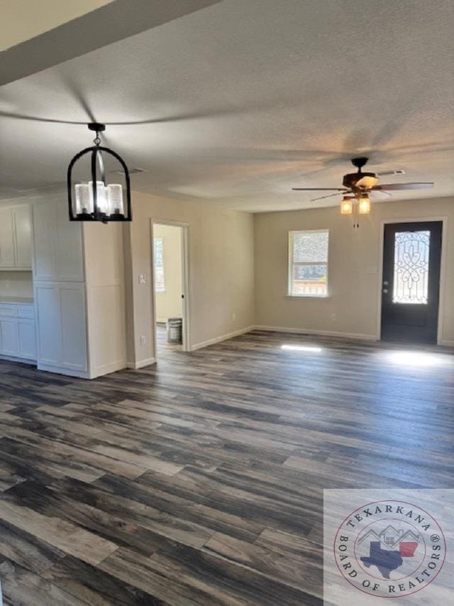 unfurnished living room featuring ceiling fan with notable chandelier, dark hardwood / wood-style floors, and a textured ceiling