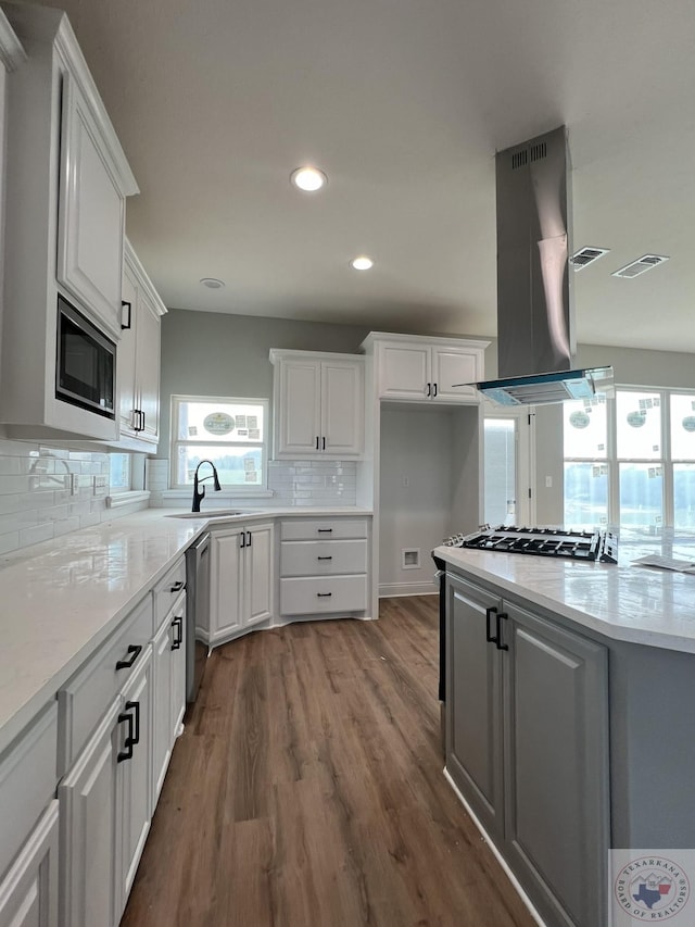 kitchen featuring built in microwave, dishwasher, white cabinetry, island exhaust hood, and decorative backsplash