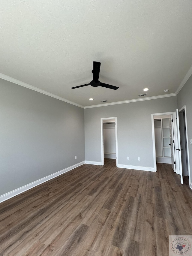 unfurnished bedroom with a walk in closet, dark hardwood / wood-style floors, a closet, ornamental molding, and ceiling fan