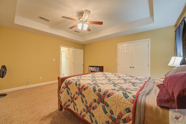 carpeted bedroom featuring ceiling fan, a tray ceiling, and a closet