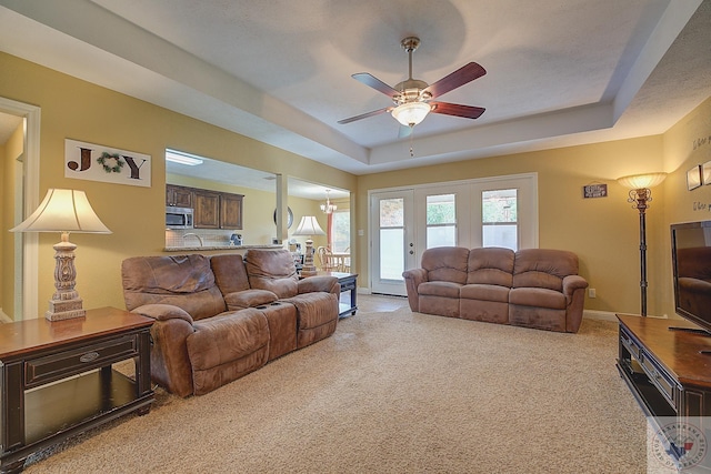 living room featuring ceiling fan, a raised ceiling, and light colored carpet