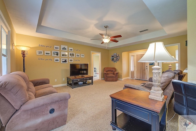 carpeted living room with ceiling fan, a raised ceiling, and a healthy amount of sunlight