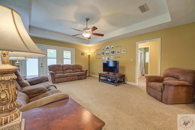 carpeted living room with ceiling fan and a tray ceiling