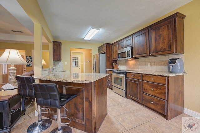 kitchen featuring kitchen peninsula, sink, tasteful backsplash, light tile patterned flooring, and stainless steel appliances