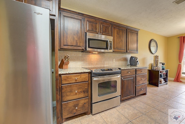 kitchen featuring light stone countertops, a textured ceiling, appliances with stainless steel finishes, backsplash, and light tile patterned floors