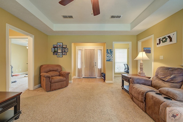 living room featuring ceiling fan, light carpet, and a raised ceiling