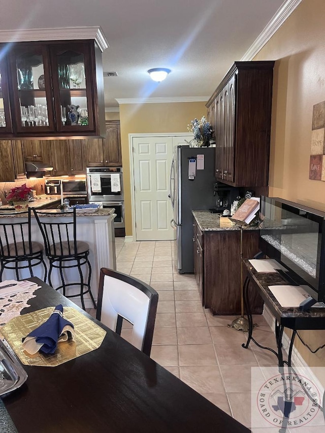 kitchen with light tile patterned floors, dark brown cabinetry, ornamental molding, and appliances with stainless steel finishes