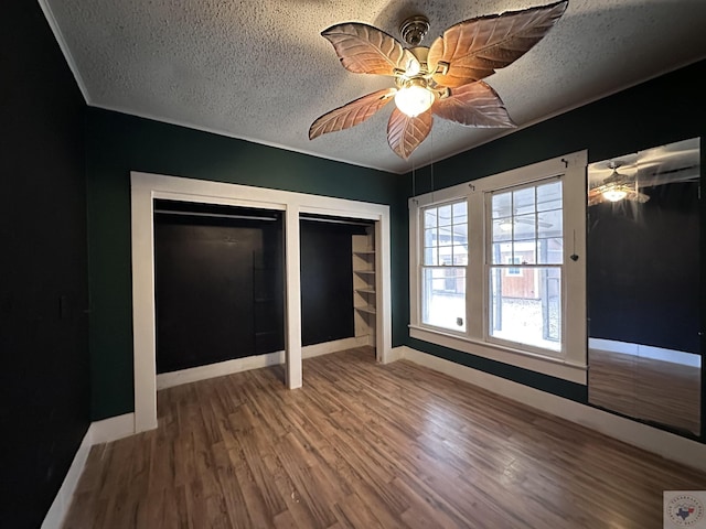 unfurnished bedroom with wood-type flooring, a textured ceiling, two closets, and ceiling fan