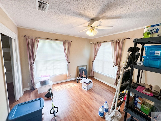 exercise room with ceiling fan, ornamental molding, a textured ceiling, and wood-type flooring