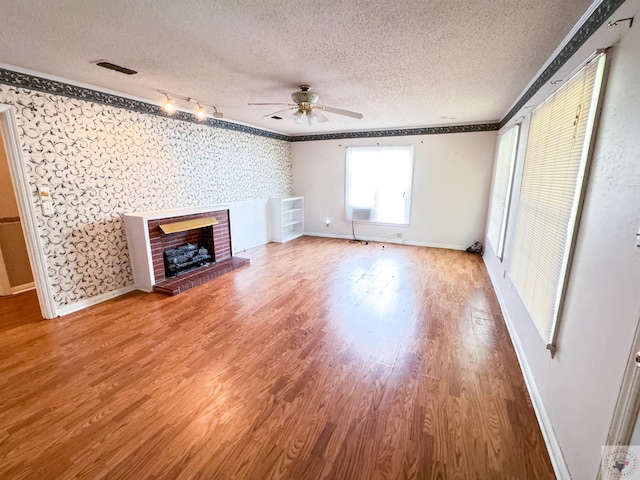 unfurnished living room featuring hardwood / wood-style flooring, ceiling fan, a fireplace, and a textured ceiling