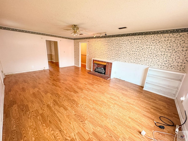 spare room with ceiling fan, a brick fireplace, a textured ceiling, and hardwood / wood-style flooring