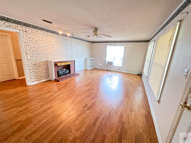 unfurnished living room with a textured ceiling, hardwood / wood-style floors, a fireplace, ornamental molding, and ceiling fan