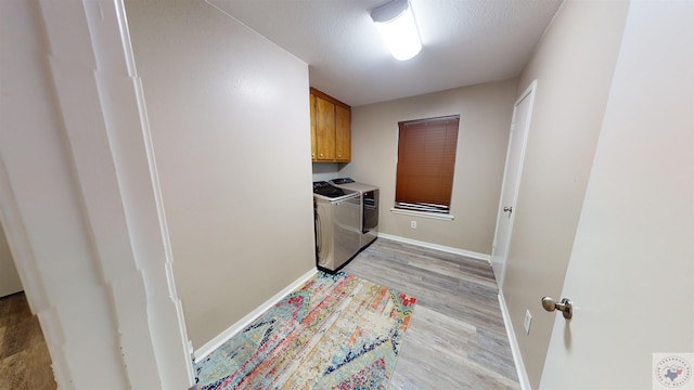 washroom featuring cabinets, light wood-type flooring, a textured ceiling, and independent washer and dryer