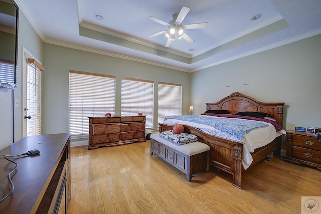 bedroom with a ceiling fan, a raised ceiling, crown molding, and light wood-type flooring