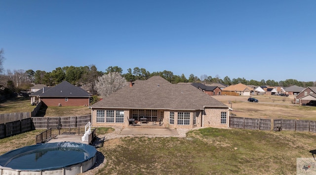 rear view of house with a lawn, a patio, a fenced backyard, a fenced in pool, and brick siding